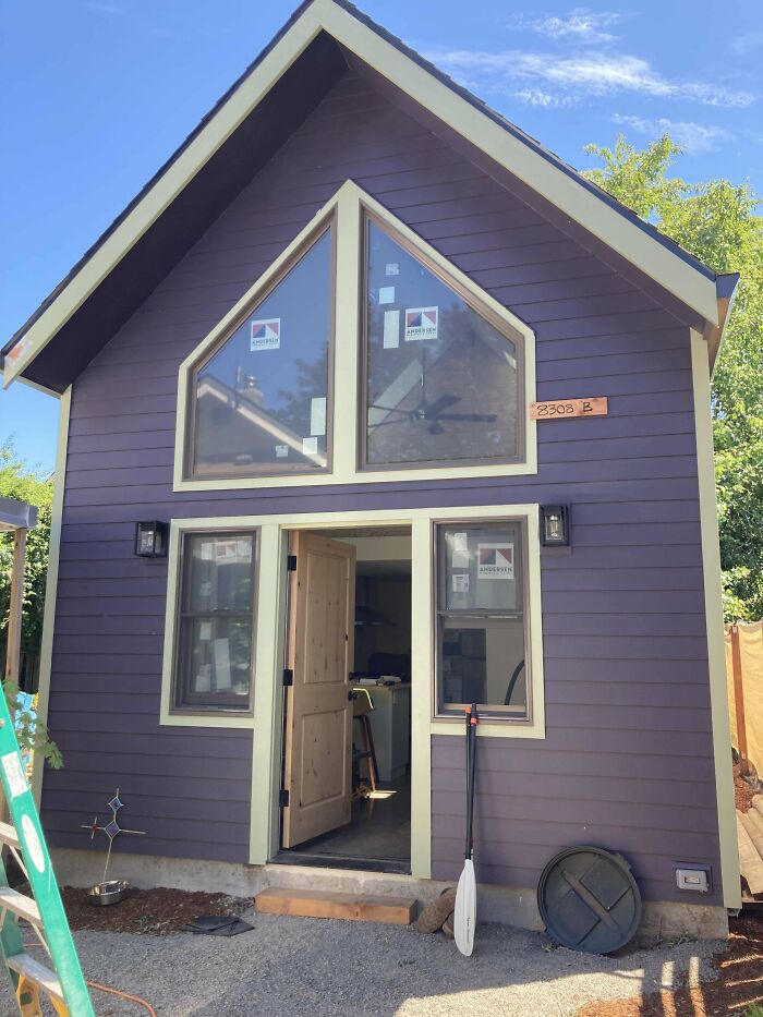 Purple tiny house design with white-trimmed windows and open door, showcasing a charming modern build.