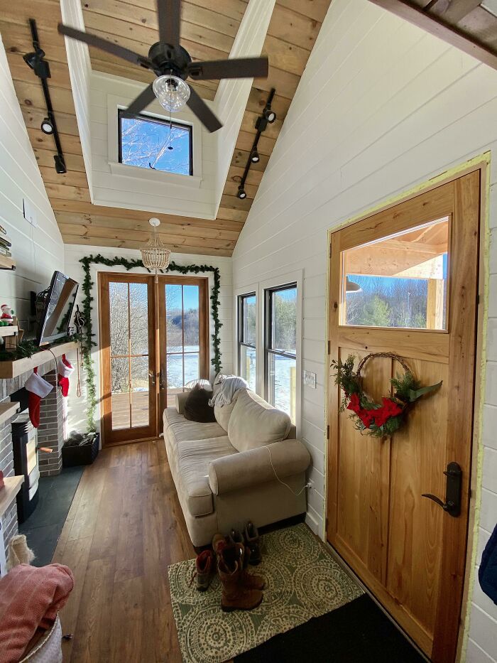 Cozy tiny house interior featuring a brown wooden door with Christmas wreath, white walls, and natural wood ceiling beams