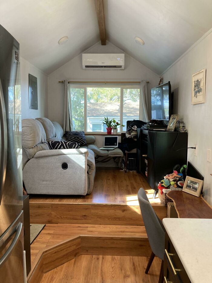 Cozy tiny house interior with wood floors, a sofa, and a TV, featuring efficient space utilization and natural light.