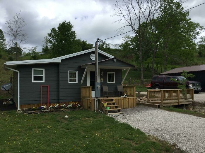 Charming tiny house with a modern gray exterior, wooden deck, and lush green surroundings.