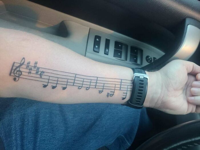 Forearm with music tattoo featuring a series of musical notes on sheet music, seen inside a car.