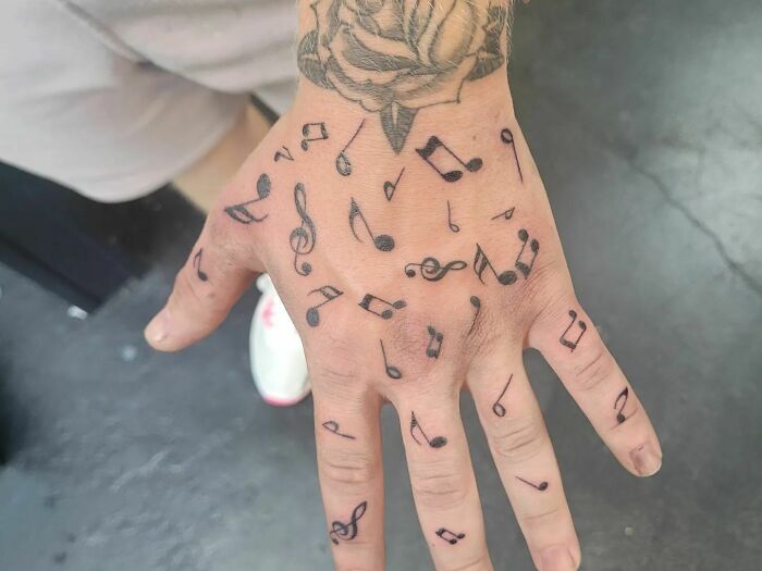 Hand with music tattoos featuring notes and a rose design.
