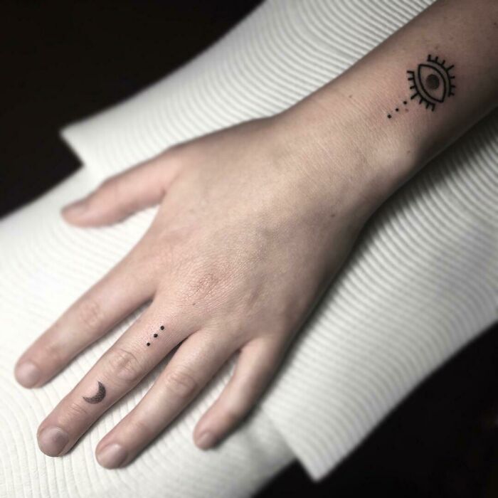 Wrist tattoo featuring an eye design with dots and a crescent moon on a finger.