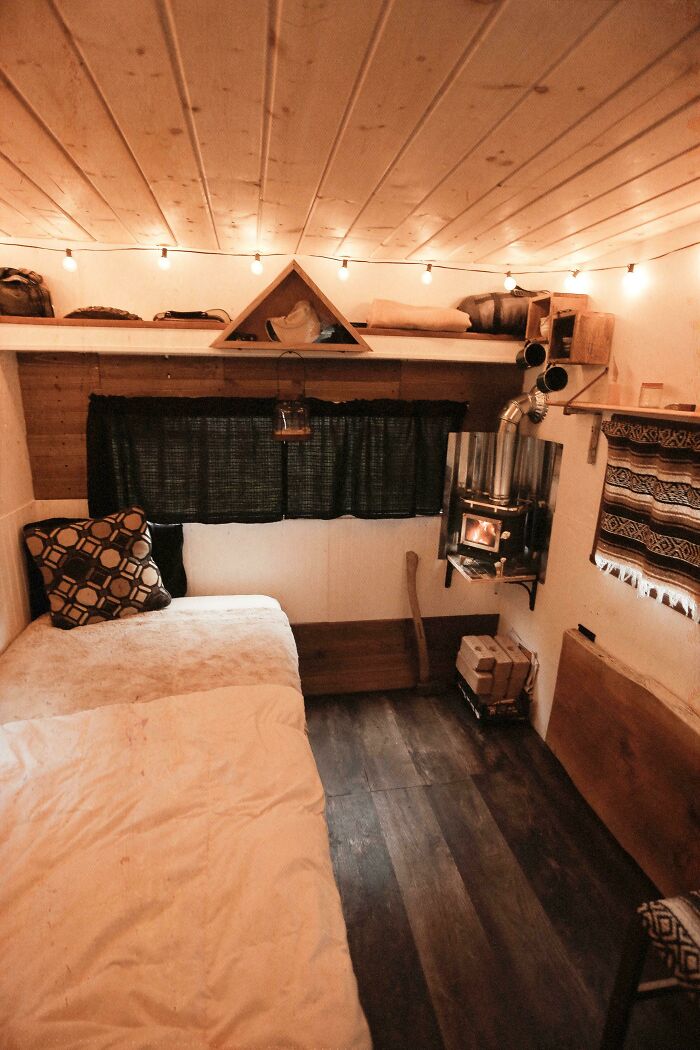 Cozy tiny house interior with wooden floors, string lights, compact living space, and a small wood stove for warmth.