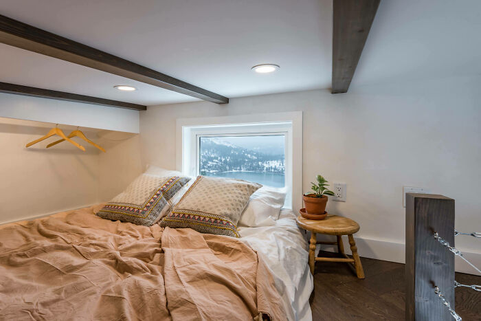 Cozy tiny house bedroom with mountain view, featuring a bed, pillows, and a small plant on a stool.