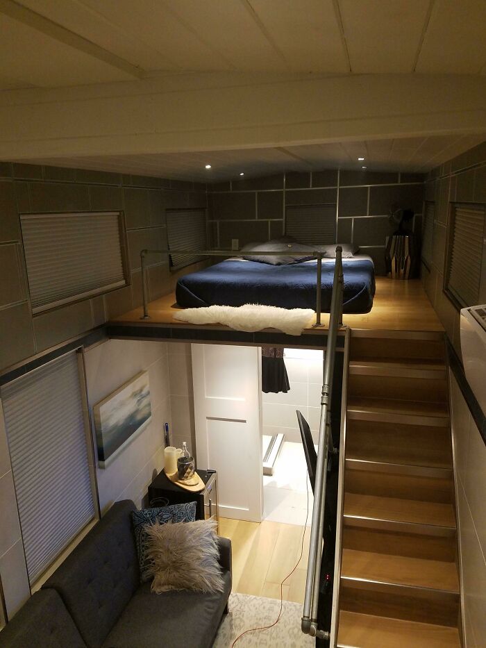 Loft bedroom in a cozy tiny house design, featuring stairs, living area, and modern decor.