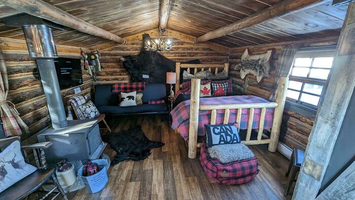Cozy tiny house bedroom with a bed featuring pink sheets and rustic wooden log cabin interior design elements.