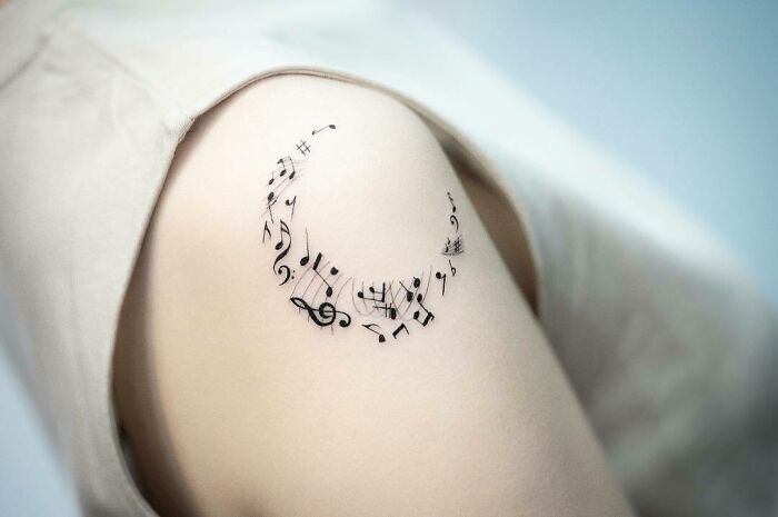 Music tattoo on an arm featuring a crescent of musical notes, showcasing unique ink design.