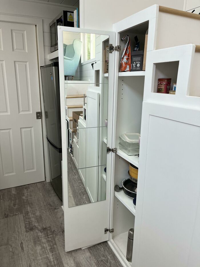 Compact and stylish tiny house design featuring a mirrored pantry door and efficient kitchen storage.
