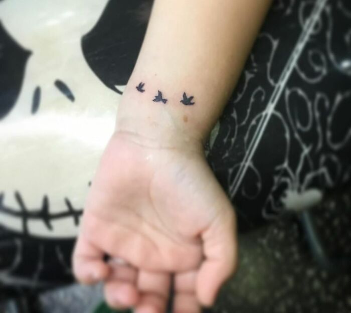 Small bird wrist tattoo design on an arm, showcasing a minimalist style.