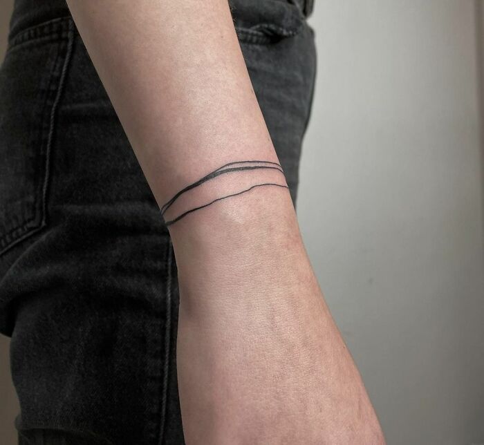 Minimalist wrist tattoo with two thin, black lines encircling the arm, illustrating simple yet striking tattoo ideas.