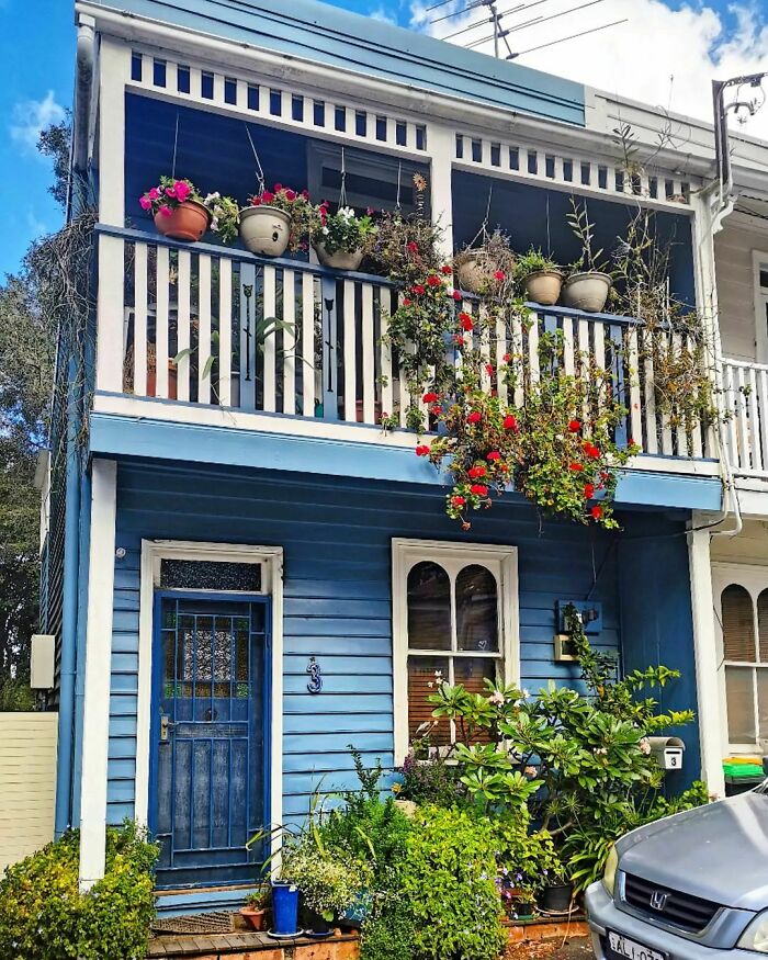 Charming tiny house with blue facade and vibrant potted plants on the balcony.