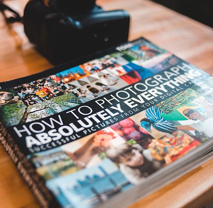 Colorful photography book with pictures, next to a camera, on a table; a great hobby to pursue for creativity.