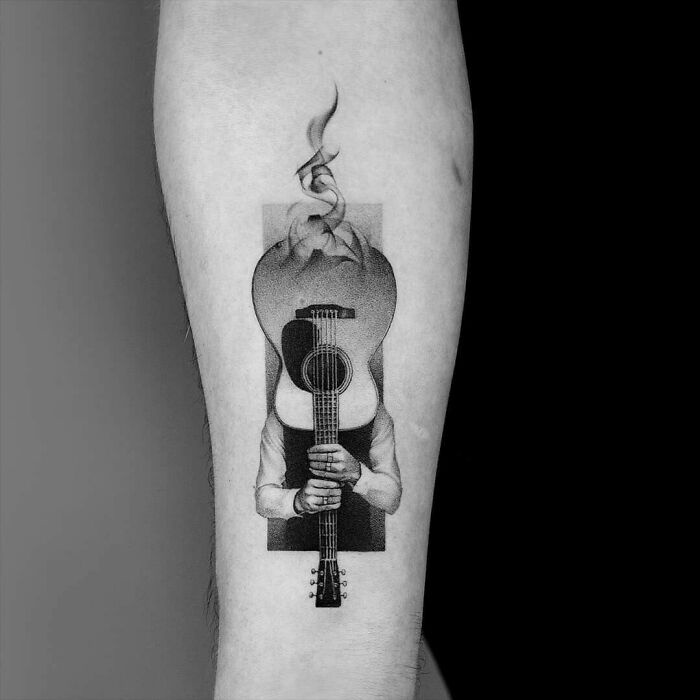 Guitar-themed music tattoo on forearm, featuring a surreal design with a person holding the instrument.