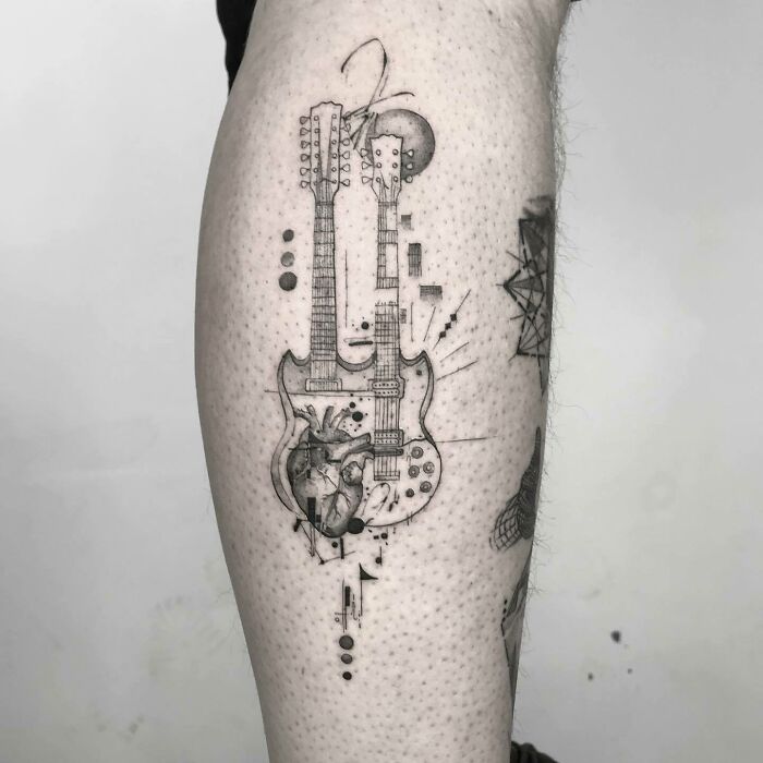 Intricate music tattoo of a double-necked guitar with a heart design on a person's arm.