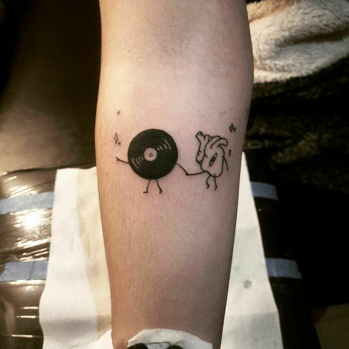 Minimalist music tattoo featuring a vinyl record and hand inking on arm, symbolizing harmony and rhythm.