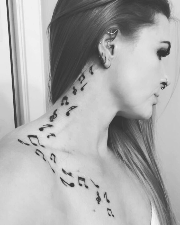 Woman with music tattoos of notes and symbols on her neck and shoulder.