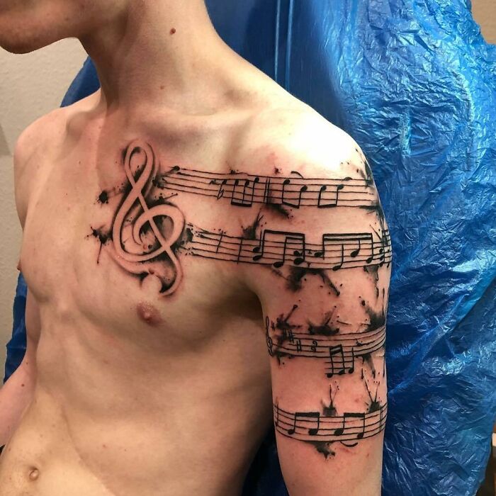 Musical notes tattoo wrapped around shoulder and arm, featuring a treble clef with ink splatter design.