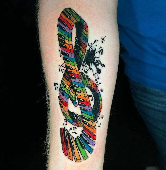 Colorful music tattoo of a treble clef with piano keys and musical notes on an arm.