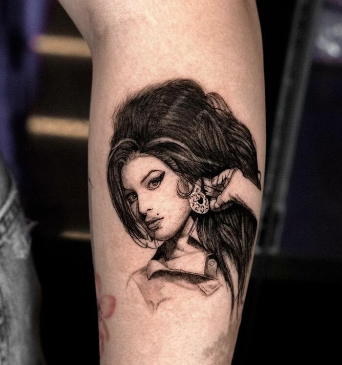 Tattoo of a woman's portrait with detailed hair and earrings, inspired by music.