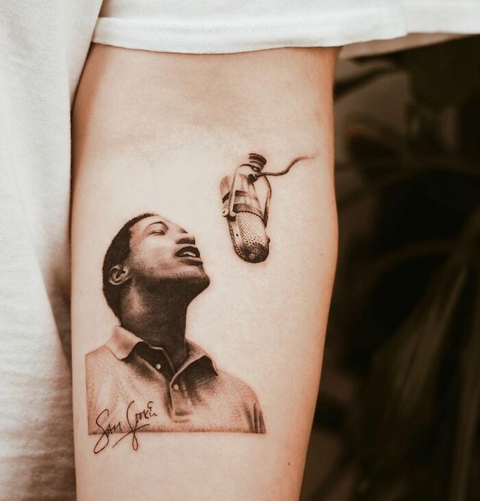 Music tattoo of a singer and vintage microphone on forearm.
