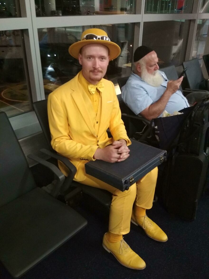 Happy man in a full yellow outfit sitting in an airport 