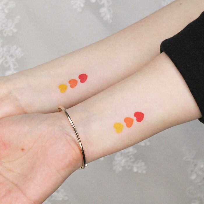 Colorful heart tattoos symbolizing family bonds on two wrists.