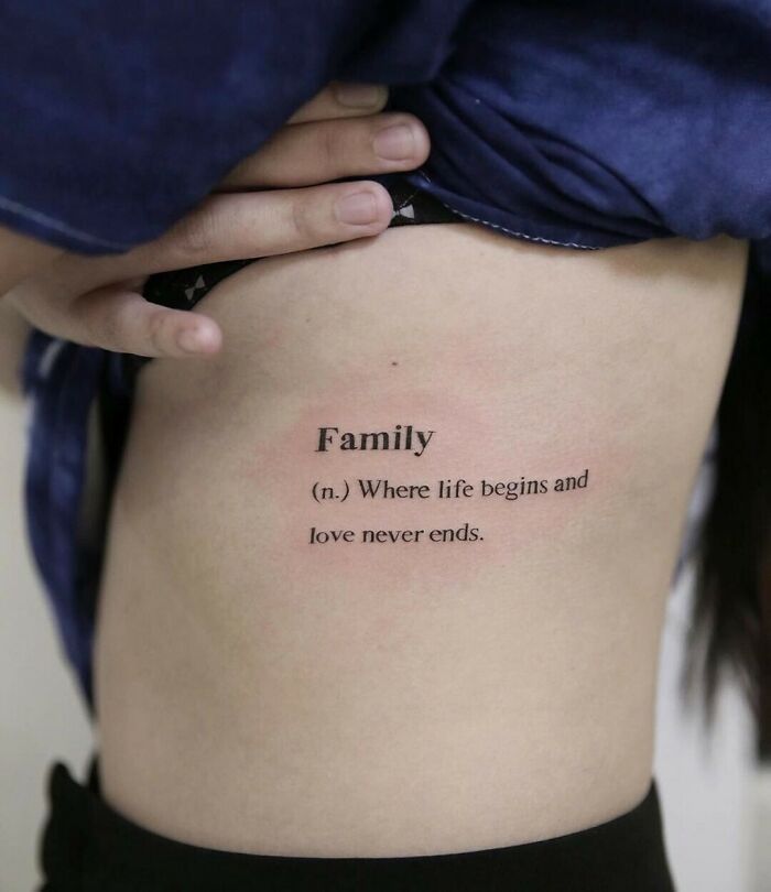Tattoo of the word "Family" with a meaningful quote on a person's side, symbolizing unbreakable family bonds.
