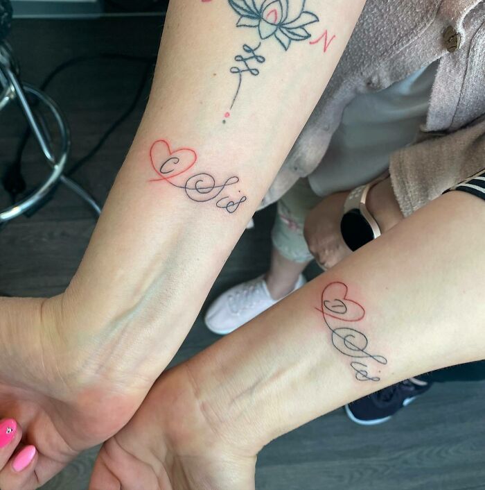Two people showing matching family tattoos with initials and heart designs on their forearms.