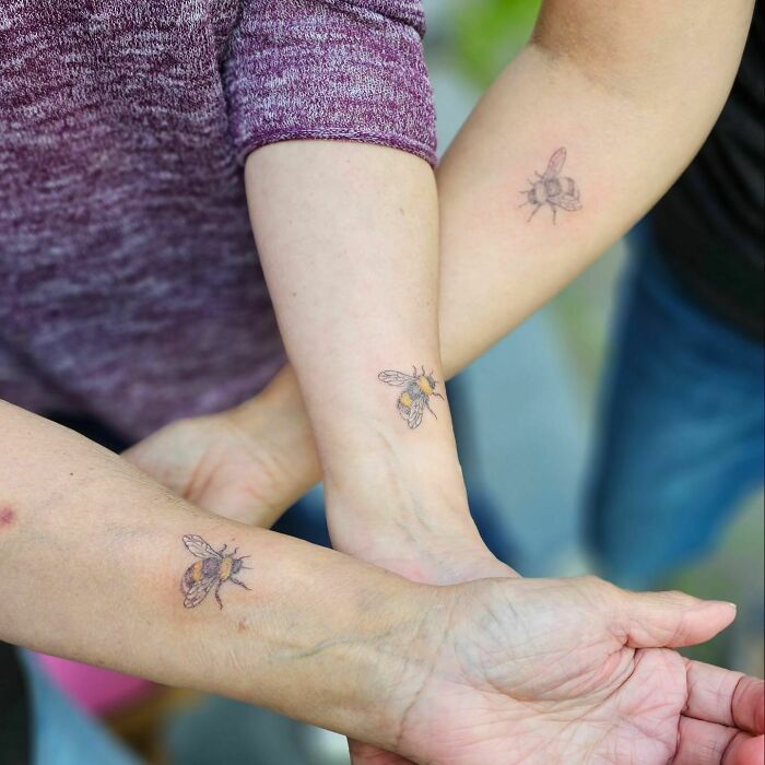 Three people showing matching bee tattoos, symbolizing family bonds and unity.