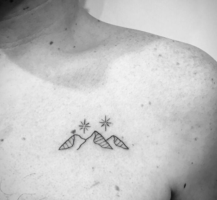 Minimalist nature tattoo of mountains and stars on a person's shoulder.