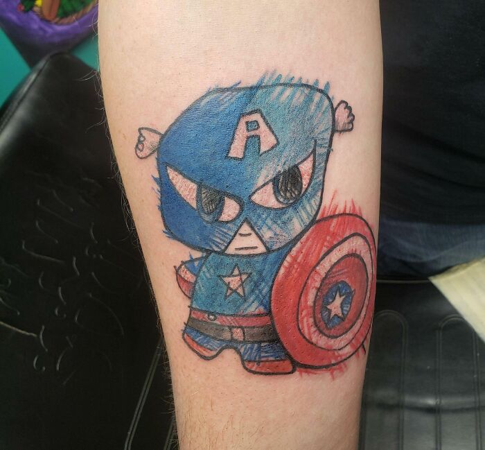 Cartoon Captain America tattoo on forearm, featuring iconic shield and blue costume.