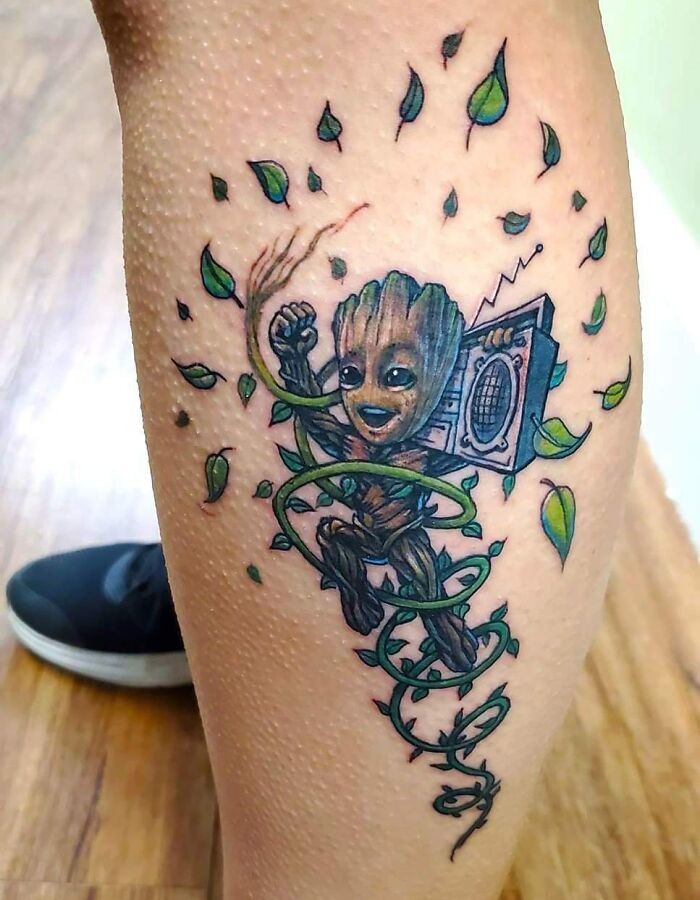 Marvel tattoo of Groot with a boombox and leaves on a leg, showcasing vibrant colors and intricate details.