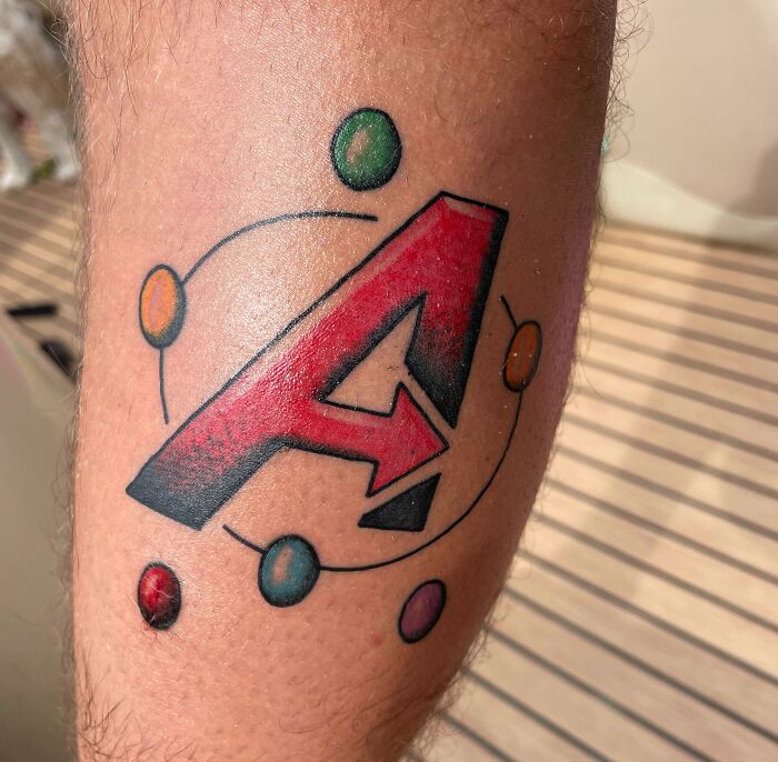 Marvel tattoo featuring a red Avengers "A" symbol with colorful Infinity Stones on a person's arm.