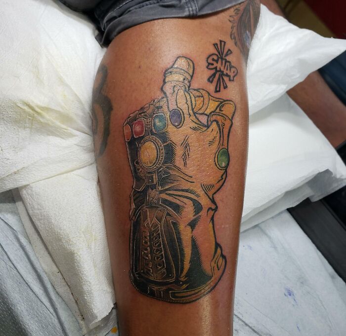 Marvel tattoo of the Infinity Gauntlet with colorful stones and "SNAP" text on a person's leg.