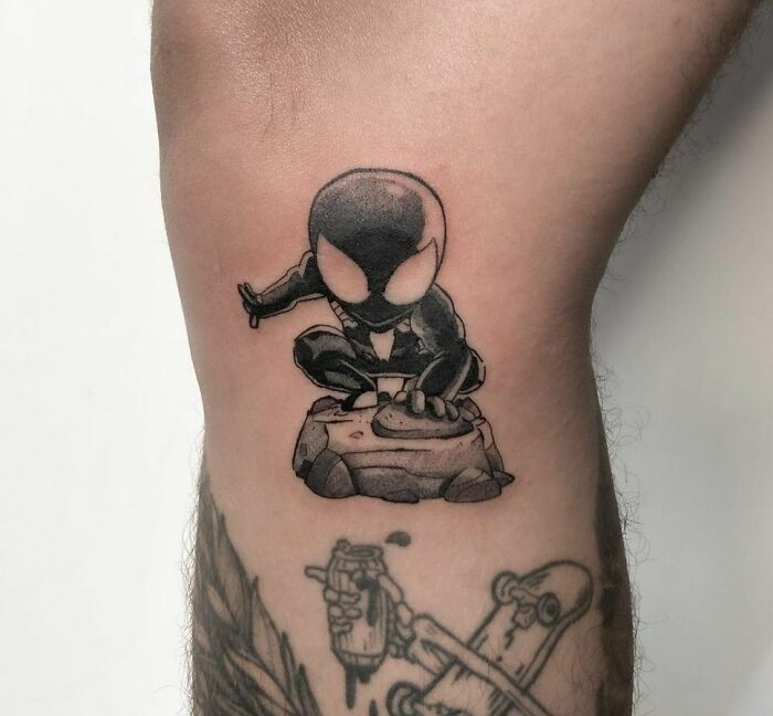 Marvel tattoo featuring a stylized character in a crouched pose on a forearm.