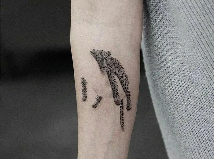 Optical illusion tattoo of a leopard appearing to emerge from the skin on a forearm.