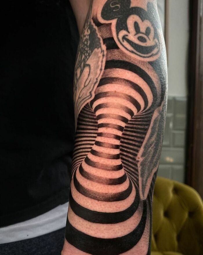 Optical illusion tattoo with a swirling black and white design on an arm, creating a 3D effect.