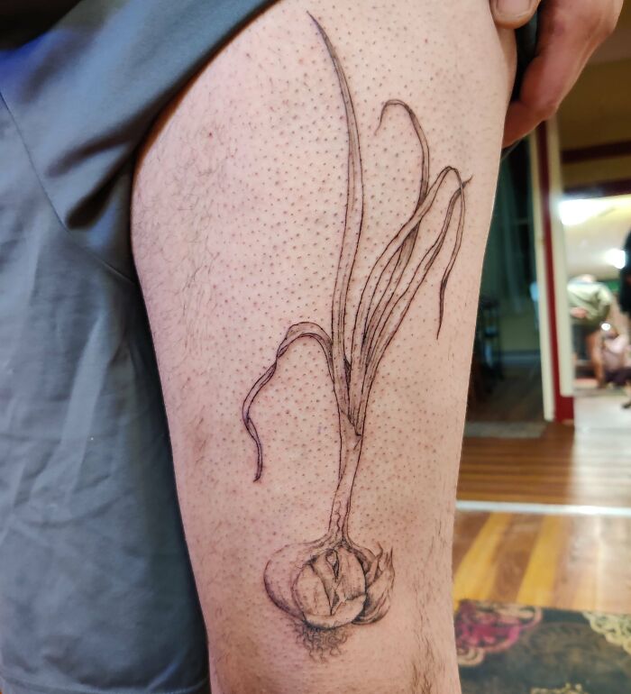 Food tattoo of a detailed garlic bulb with roots and leaves inked on a person's leg.
