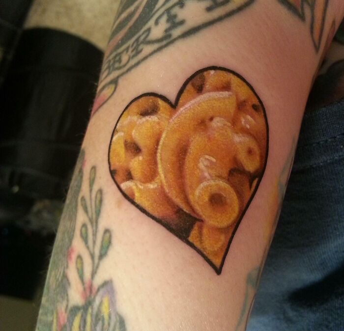 Heart-shaped food tattoo featuring macaroni and cheese design on an arm.