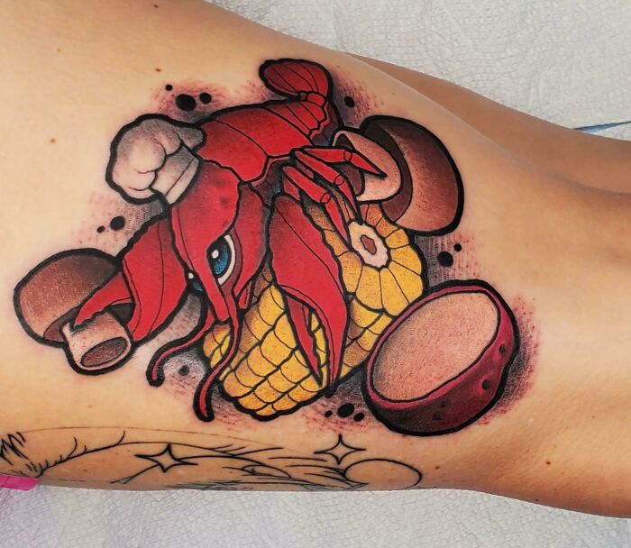 Food tattoo of a lobster, corn, and sausage on skin, showcasing vibrant colors and intricate detail.