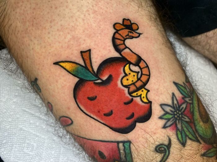 Watercolor tattoo of a bitten red apple with a worm, showcasing food-inspired ink-spiration on skin.