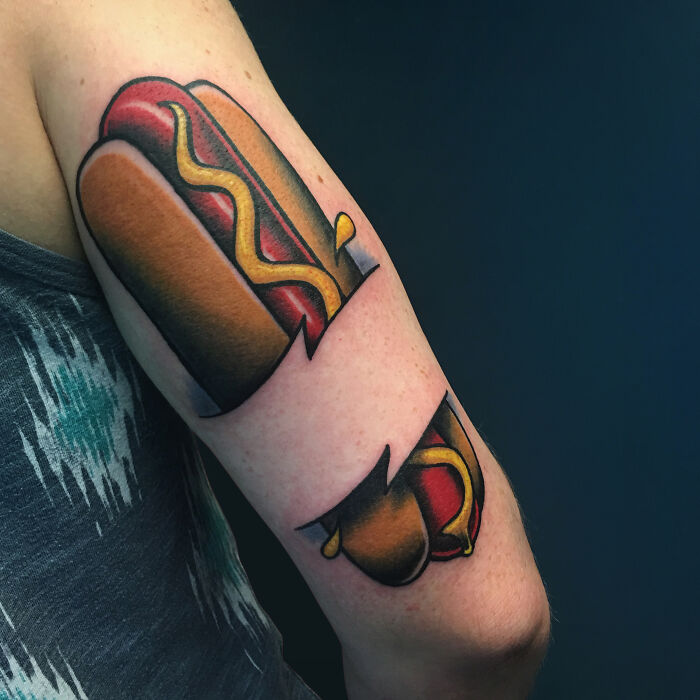Tattoo of a hotdog with mustard and ketchup on an arm, showcasing delicious food-inspired ink design.
