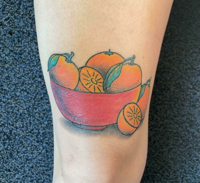 Food tattoo of oranges in a red bowl on skin.