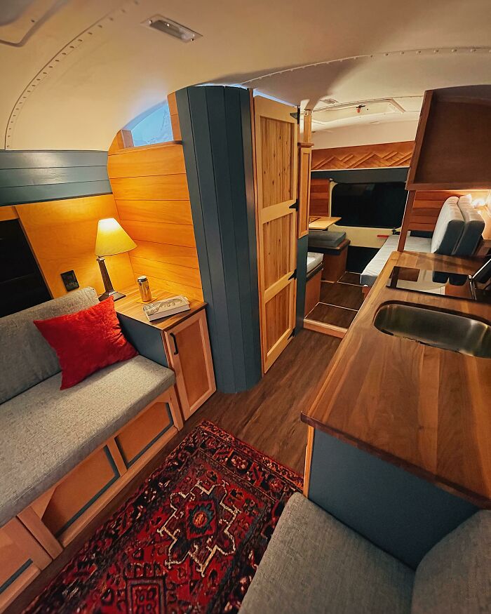 Cozy tiny house design interior with wooden countertop, grey couch, red pillow, warm lighting, and compact living space.