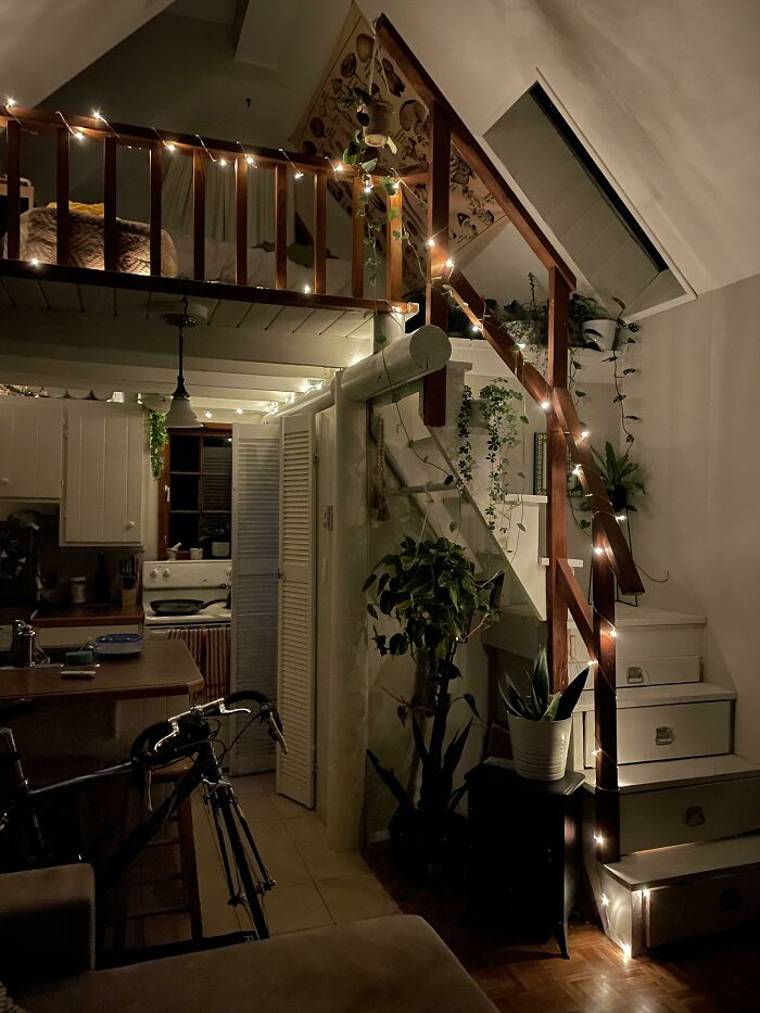 Cozy wooden stairs with string lights in a tiny house design featuring plants and warm ambient lighting.