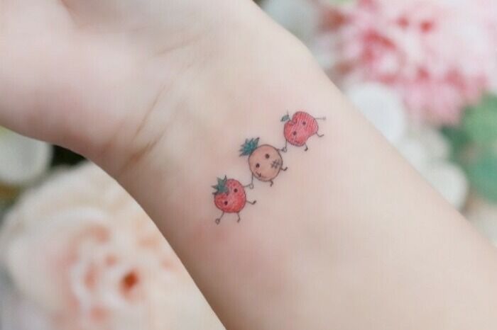 Tattoo of three small, cute strawberries on a wrist, symbolizing the mother-child bond.