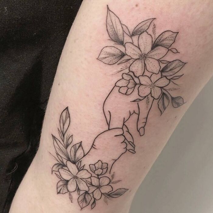 Mother-child bond tattoo with flowers and intertwined hands.