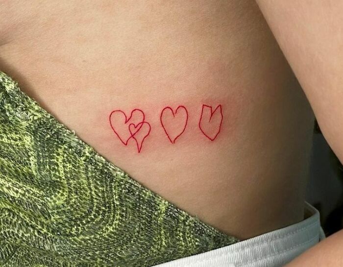 Red ink tattoos of heart outlines on a person's side, close-up view.