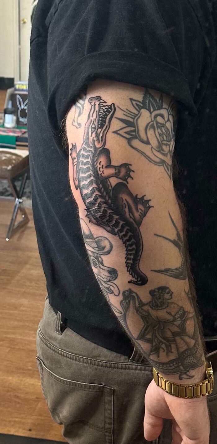 Arm with an American traditional tattoo featuring a crocodile and floral designs.